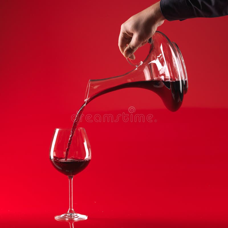 Man's hand pouring red wine from decanter in glass, on red background. Man's hand pouring red wine from decanter in glass, on red background