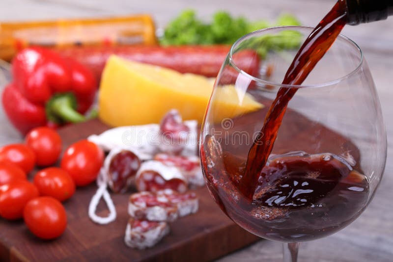 Pouring red wine into glass and food background. Pouring red wine into glass and food background