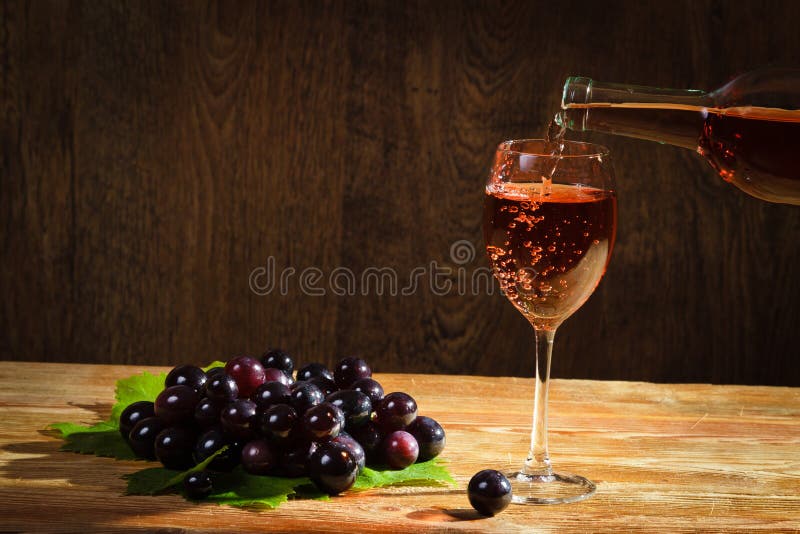 Vinho vermelho que derrama para baixo ao vidro com uvas