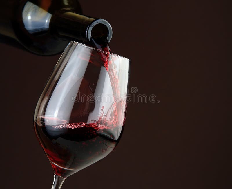 Vino rosso di versamento su fondo scuro fotografia stock Vino rosso di versamento su fondo scuro fotografia stock