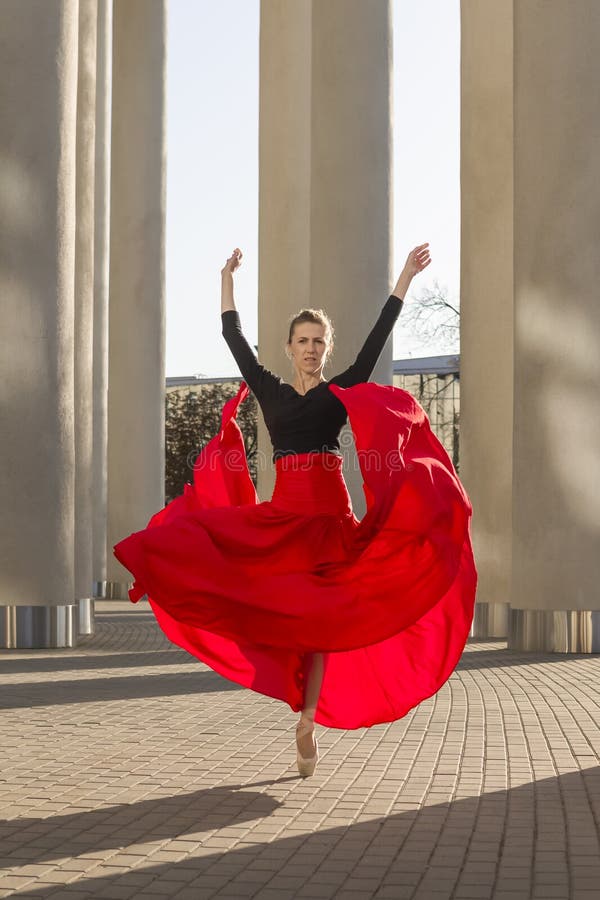 Vinsome caucasian ballet dancer i röd klänning som i rött kjolt är i dansställning med lyft hand royaltyfri foto