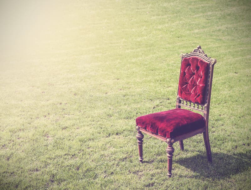 Vintage antique old red chair on green grass, abstract background.