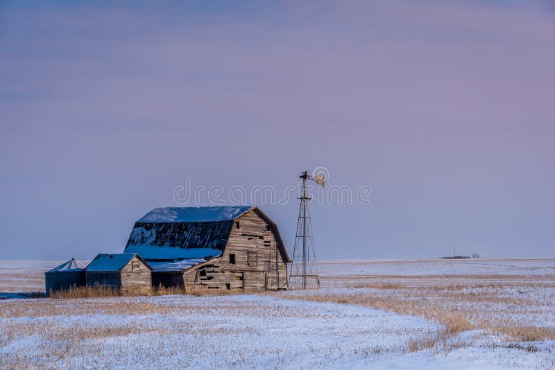 Vintage barn, bins and windmill surrounded by snow under pink sunset sky in Saskatchewan