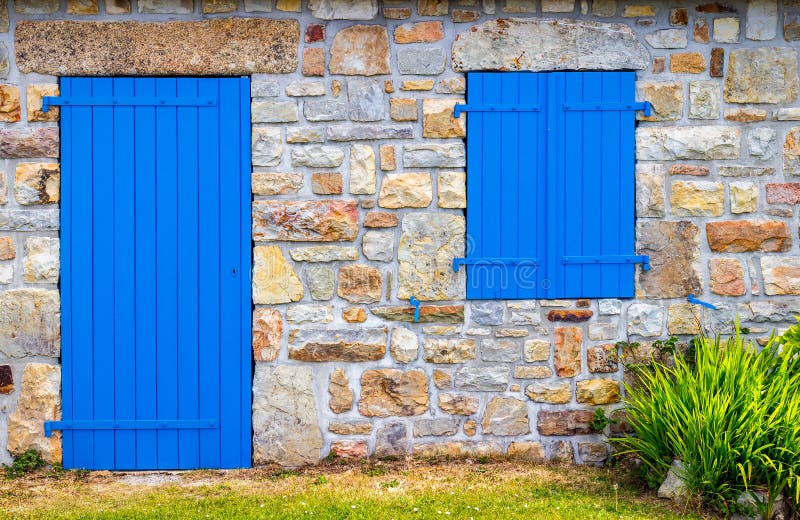 Vintage blue door and window on the facade of an old cottage stone wall.