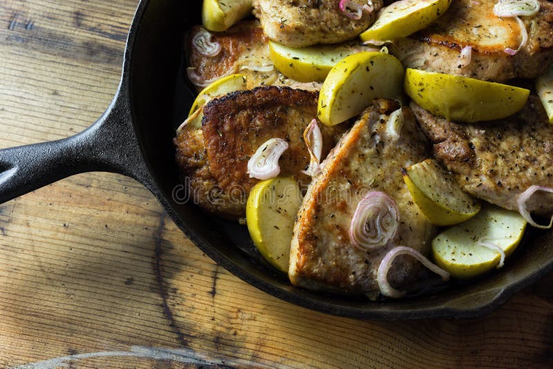 Pork chops with sliced onions and granny smith apples in a cast iron skillet.