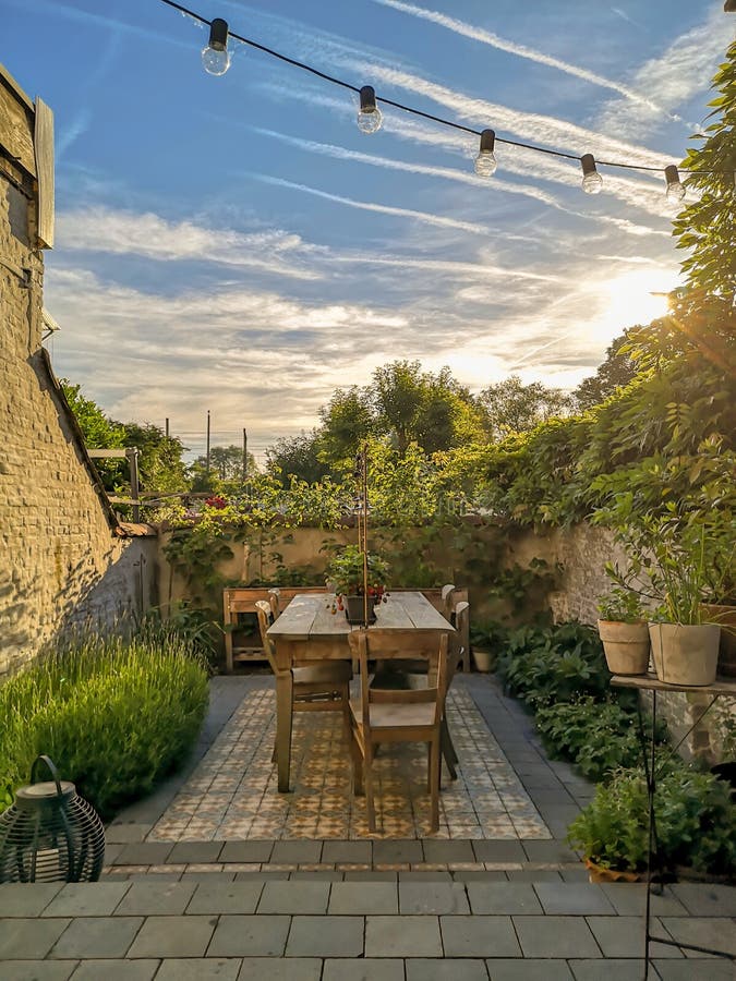 Vintage cement tiles in a small walled urban garden full with green plants and wooden furniture in summer during sunrise royalty free stock image Vintage cement tiles in a small walled urban garden full with green plants and wooden furniture in summer during sunrise royalty free stock image