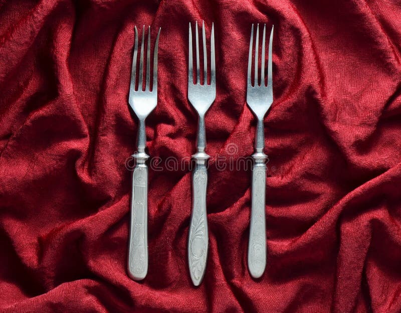 Vintage forks on a red silk tablecloth. Top view.