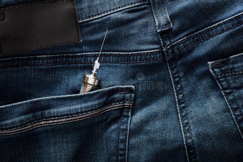 Vintage injector syringe in the back pocket of blue jeans. Drug and heroine addiction problem among the youth