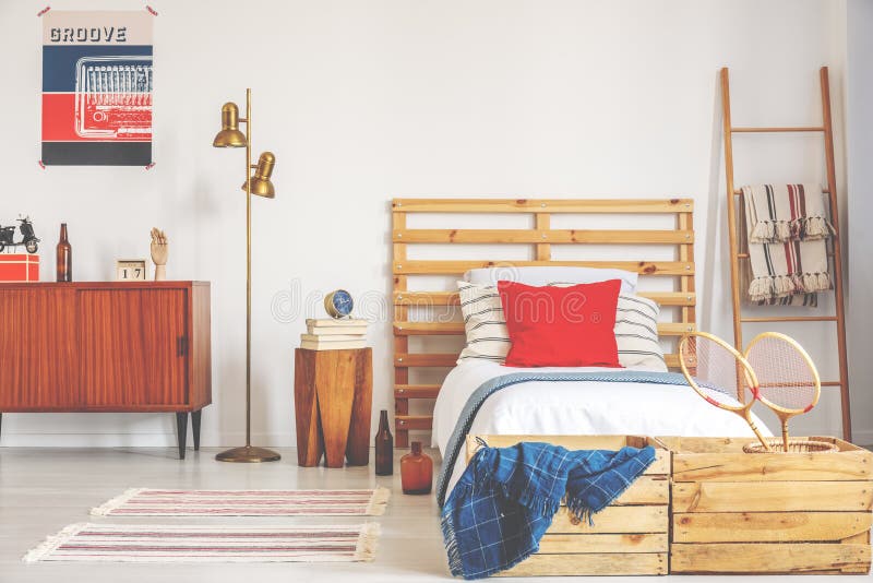 Vintage poster and cabinet next to golden lamp and wooden bed with bedside table with books and clock