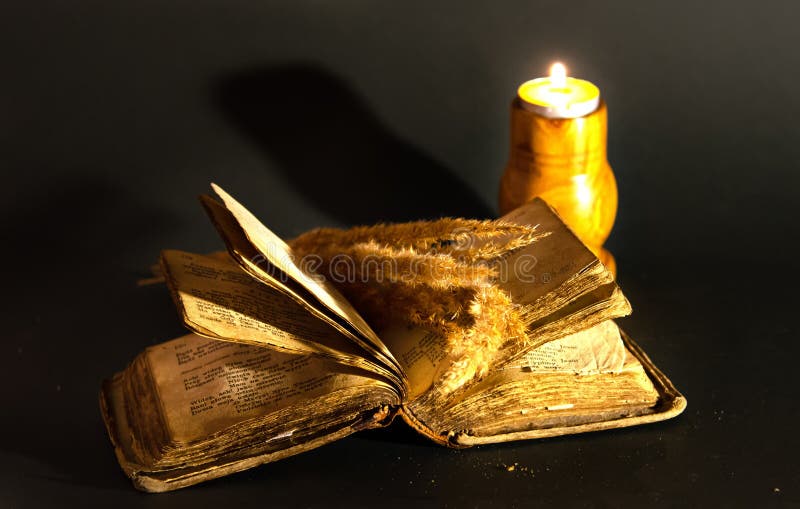 Vintage still life with a lit candle near an old book at night