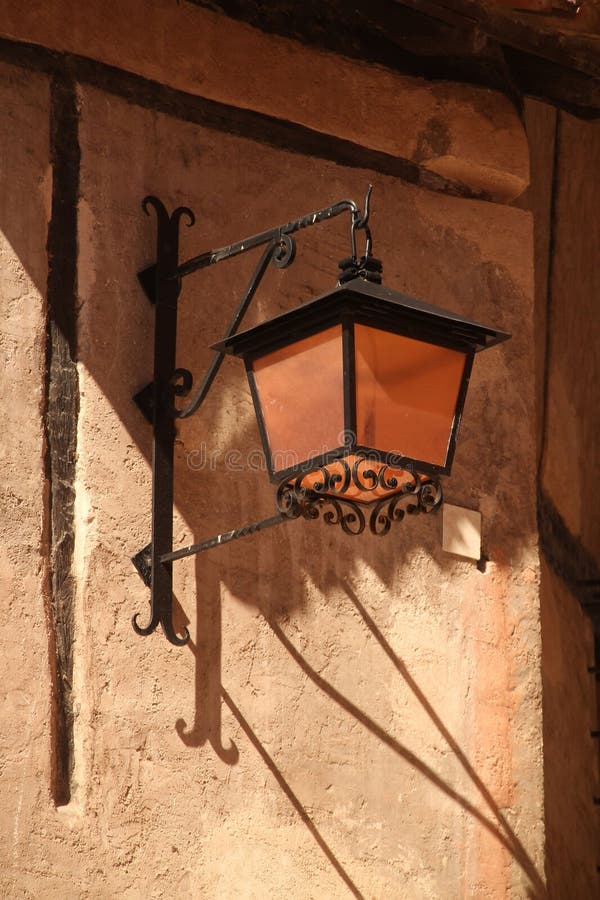 Vintage wall-mounted lantern casting shadows on a textured wall in daylight. Albarracin, Spain stock photo