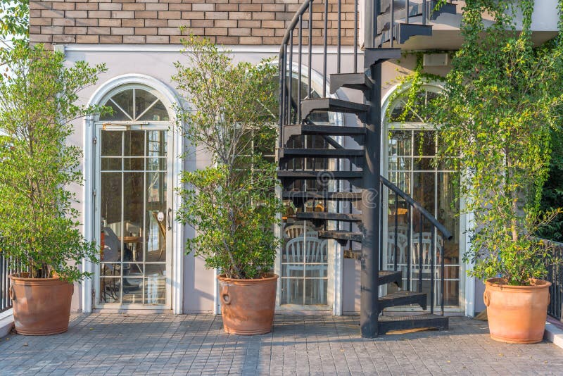 Vintage white frame door and modern black metal spiral staircase with natural green tree gardening exterior for home and living ac