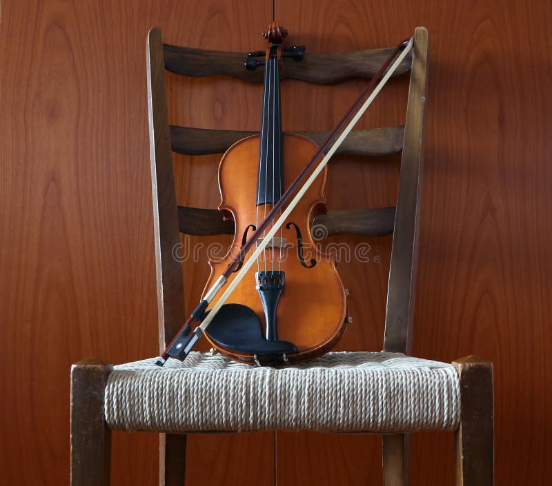 Violon avec l'arc sur une chaise avec un siège de paille Fond en bois de mur images libres de droits Violon avec l'arc sur une chaise avec un siège de paille Fond en bois de mur images libres de droits