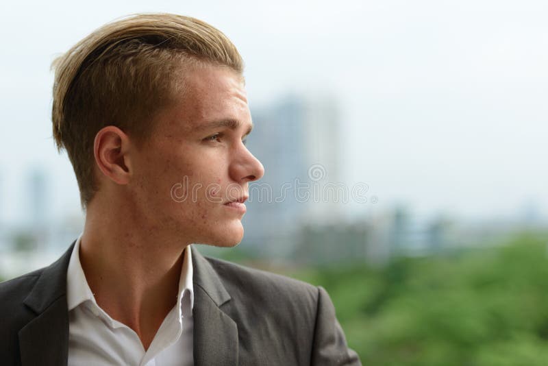Vista de perfil de um homem bonito com cabelo loiro olhando para a câmera  ao ar livre