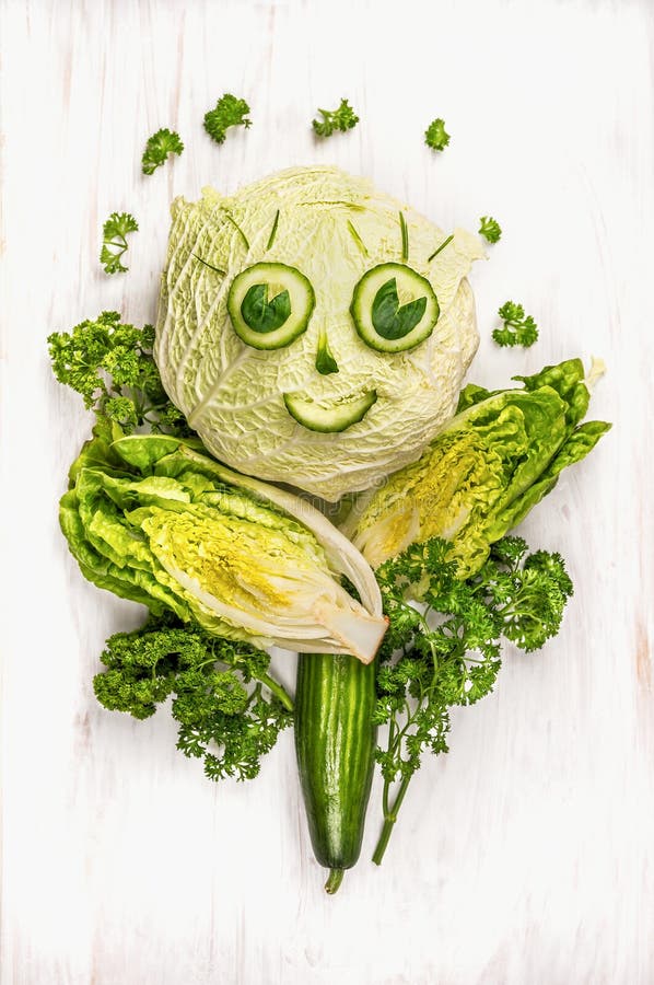 Visage drôle de fille fait en légumes, concombre et laitue verts sur en bois blanc photographie stock libre de droits Visage drôle de fille fait en légumes, concombre et laitue verts sur en bois blanc photographie stock libre de droits