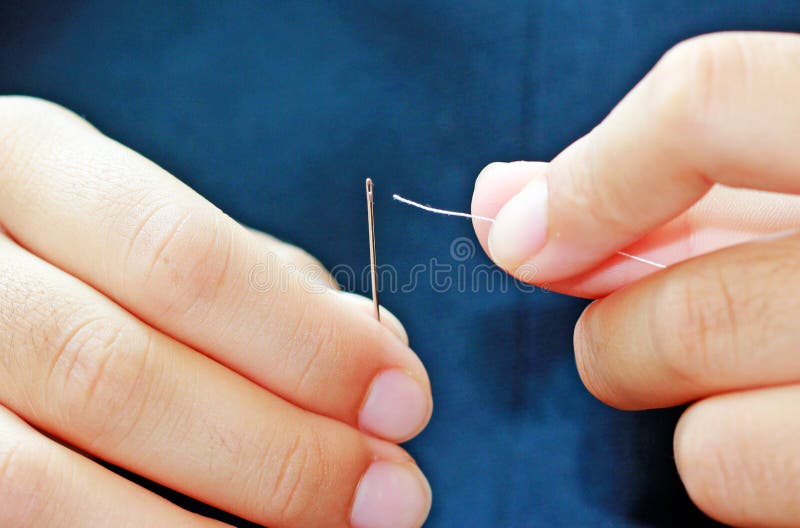 Fingers inserting thread into a needle. Fingers inserting thread into a needle.