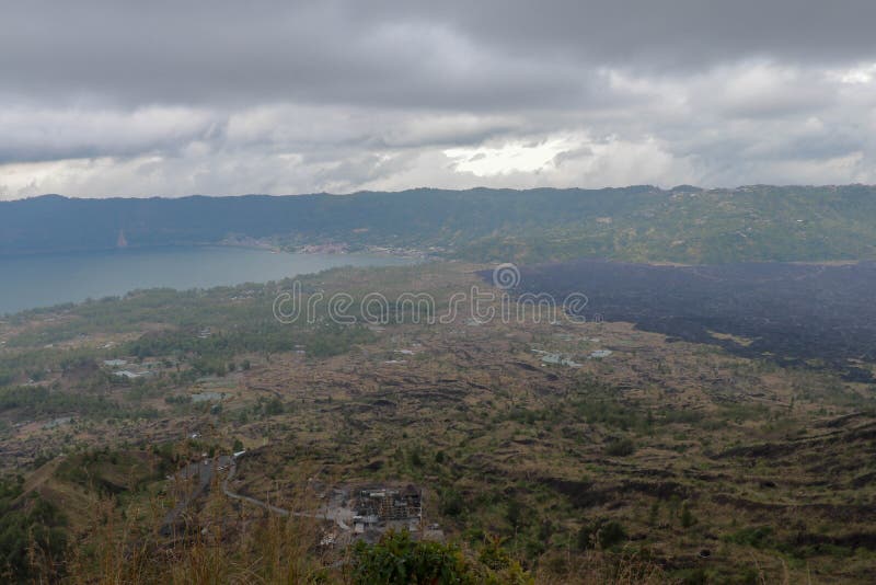 Visión desde la montaña majestuosa de Gunung Batur a la caldera volcánica con el lago y el campo de lava negro Cielo cubierto con imagen de archivo libre de regalías Visión desde la montaña majestuosa de Gunung Batur a la caldera volcánica con el lago y el campo de lava negro Cielo cubierto con imagen de archivo libre de regalías