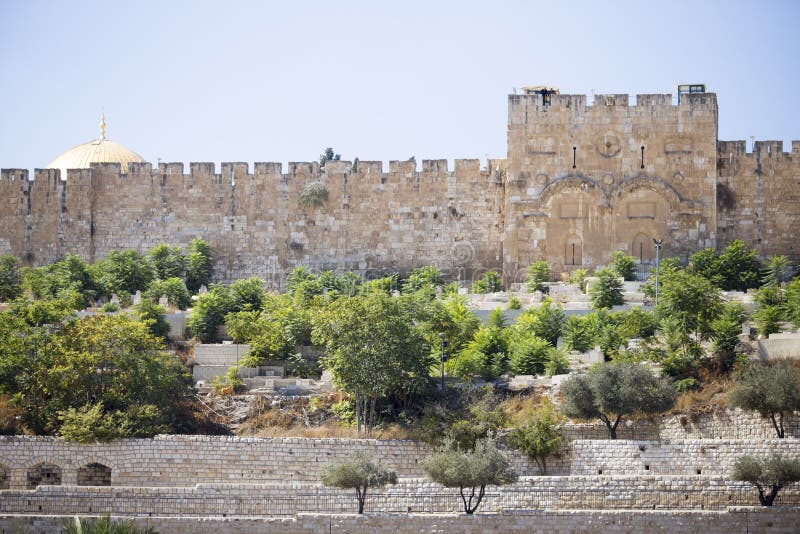 View from afar on ancient stone walls surrounded by trees and the Golden Gate of Jerusalem against the blue cloudless sky. View from afar on ancient stone walls surrounded by trees and the Golden Gate of Jerusalem against the blue cloudless sky