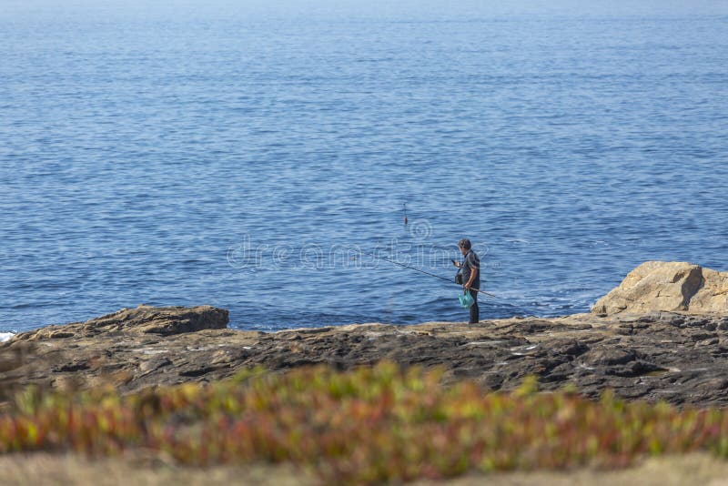Visión en el mar de las aguas y el acantilado de rocas, con un pescador y las cañas de pescar, en la costa foto de archivo libre de regalías Visión en el mar de las aguas y el acantilado de rocas, con un pescador y las cañas de pescar, en la costa foto de archivo libre de regalías