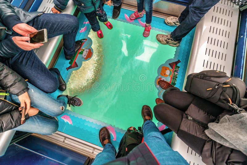 Hong Kong - January 26, 2016: Ocean shore viewed through the glass floor of a Crystal Cabin full of people, Ngong Ping 360 Skyrail on Lantau Island, Hong Kong. Tourists ride on gondola lift. Hong Kong - January 26, 2016: Ocean shore viewed through the glass floor of a Crystal Cabin full of people, Ngong Ping 360 Skyrail on Lantau Island, Hong Kong. Tourists ride on gondola lift