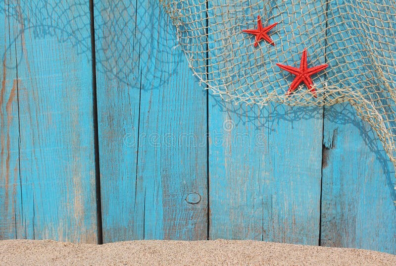 Fishing net and red starfishes against an old blue wooden background and sand. Fishing net and red starfishes against an old blue wooden background and sand