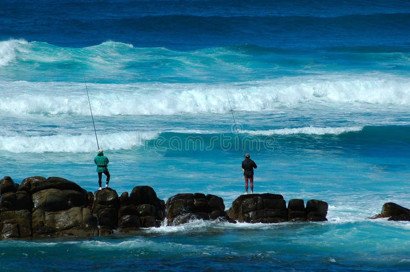 Two active anglers fishing in the Indian Ocean during high tide at Schoenmakerskop Beach, Port Elizabeth, South Africa. Two active anglers fishing in the Indian Ocean during high tide at Schoenmakerskop Beach, Port Elizabeth, South Africa