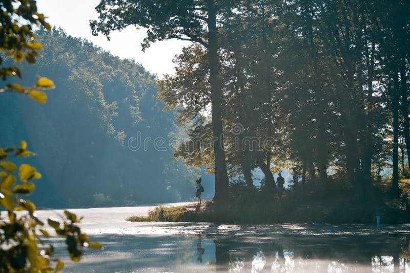 Visserssilhouetten op een bank van weinig natuurlijk meer in zonsopgang van de bos, mistige ochtend de mooie zomer, backlight aar royalty-vrije stock afbeeldingen Visserssilhouetten op een bank van weinig natuurlijk meer in zonsopgang van de bos, mistige ochtend de mooie zomer, backlight aar royalty-vrije stock afbeeldingen