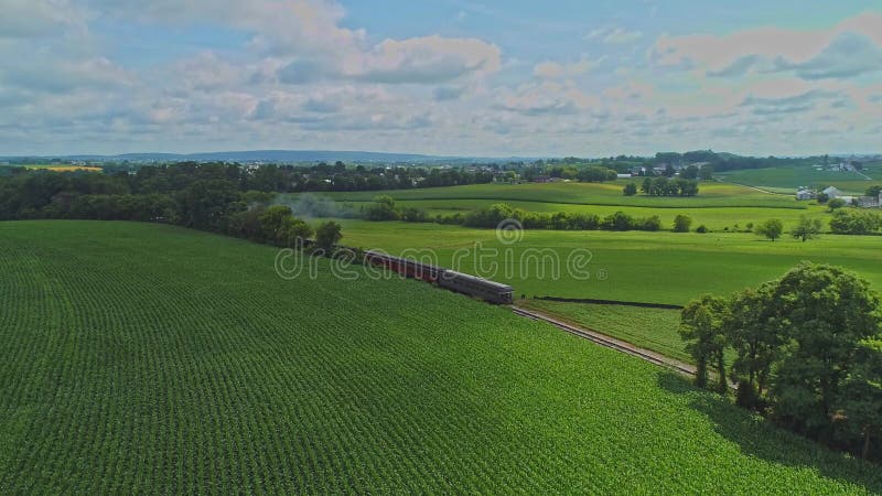 Vista aerea dei campi di mais e dei raccolti di colata con un treno passeggeri che viaggia attraverso di esso