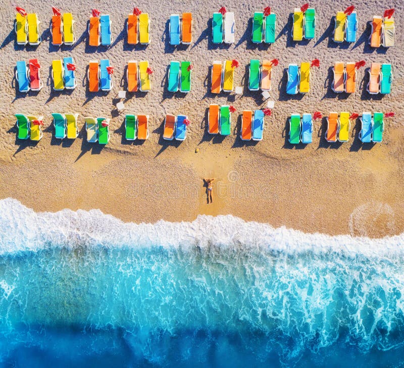 Vista aerea della donna di menzogne sulla spiaggia con le chaise longue variopinte immagine stock Vista aerea della donna di menzogne sulla spiaggia con le chaise longue variopinte immagine stock
