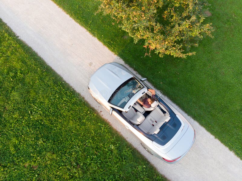 Vista aerea di riuscito uomo che conduce e che gode della sua automobile sportiva di lusso del convertibile d'argento dal lato de fotografie stock libere da diritti Vista aerea di riuscito uomo che conduce e che gode della sua automobile sportiva di lusso del convertibile d'argento dal lato de fotografie stock libere da diritti