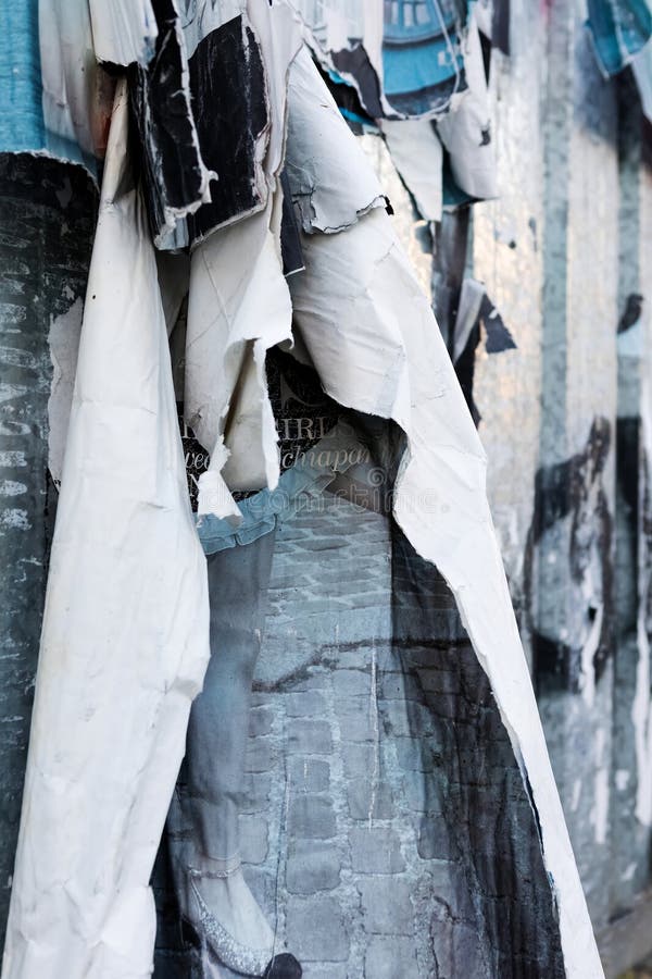 Close-up view of a torn street poster on a grey background, revealing a glimpse of a blue sky through the tears. Abstract urban art featuring fragments of black text on a white background. Close-up view of a torn street poster on a grey background, revealing a glimpse of a blue sky through the tears. Abstract urban art featuring fragments of black text on a white background