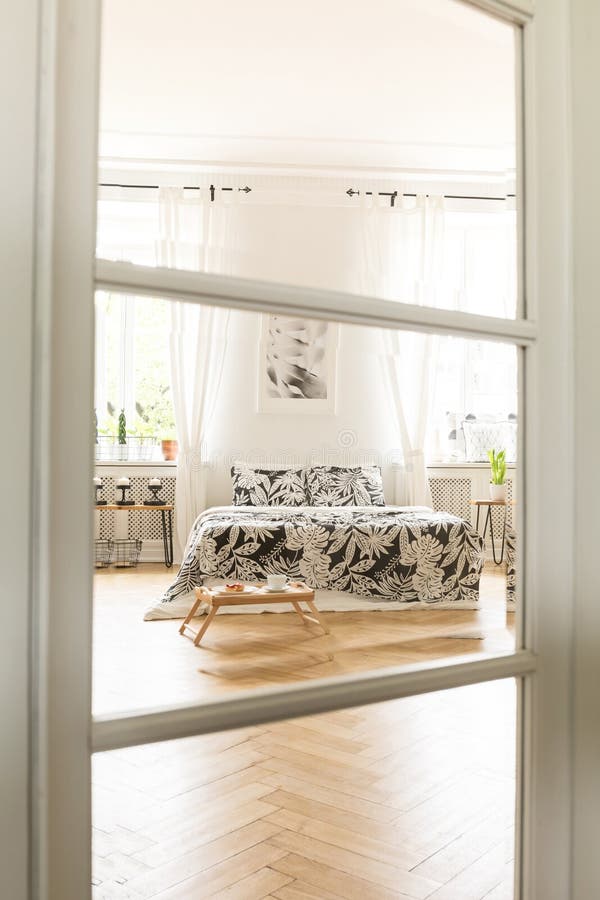Vista attraverso una porta di vetro e di legno ad un interno bianco spazioso della camera da letto con un letto con tela che sta immagine stock libera da diritti