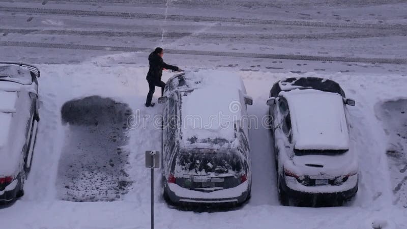 Vista aérea de la mujer limpiando la nieve y el hielo de la ventana del escudo de viento de su auto en la fría tormenta de nieve e