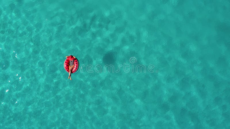 Aerial view of slim woman swimming on the swim ring donut in the transparent turquoise sea in Seychelles. Summer seascape with girl, beautiful waves, colorful water. Top view from drone. Aerial view of slim woman swimming on the swim ring donut in the transparent turquoise sea in Seychelles. Summer seascape with girl, beautiful waves, colorful water. Top view from drone