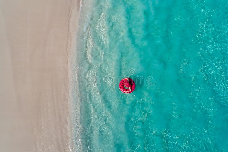 Aerial view of slim woman swimming on the swim ring donut in the transparent turquoise sea in Seychelles. Summer seascape with girl, beautiful waves, colorful water. Top view from drone. Aerial view of slim woman swimming on the swim ring donut in the transparent turquoise sea in Seychelles. Summer seascape with girl, beautiful waves, colorful water. Top view from drone
