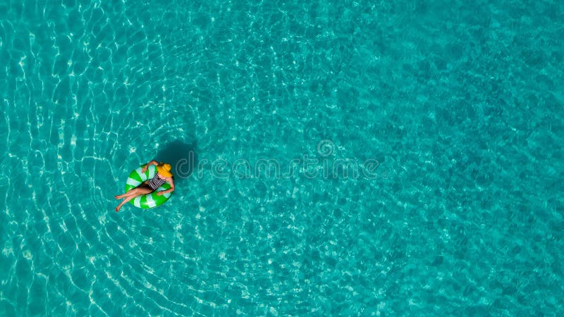 Aerial view of slim woman swimming on the swim ring donut in the transparent turquoise sea in Seychelles. Summer seascape with girl, beautiful waves, colorful water. Top view from drone. Aerial view of slim woman swimming on the swim ring donut in the transparent turquoise sea in Seychelles. Summer seascape with girl, beautiful waves, colorful water. Top view from drone