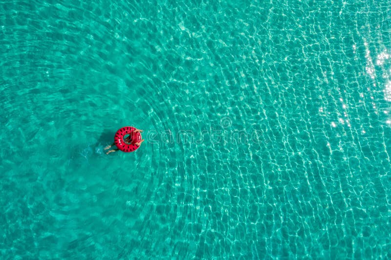 Aerial view of slim woman swimming on the swim ring donut in the transparent turquoise sea in Seychelles. Summer seascape with girl, beautiful waves, colorful water. Top view from drone. Aerial view of slim woman swimming on the swim ring donut in the transparent turquoise sea in Seychelles. Summer seascape with girl, beautiful waves, colorful water. Top view from drone