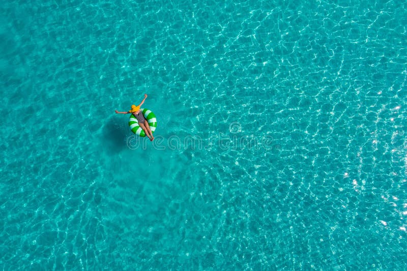 Aerial view of slim woman swimming on the swim ring donut in the transparent turquoise sea in Seychelles. Summer seascape with girl, beautiful waves, colorful water. Top view from drone. Aerial view of slim woman swimming on the swim ring donut in the transparent turquoise sea in Seychelles. Summer seascape with girl, beautiful waves, colorful water. Top view from drone