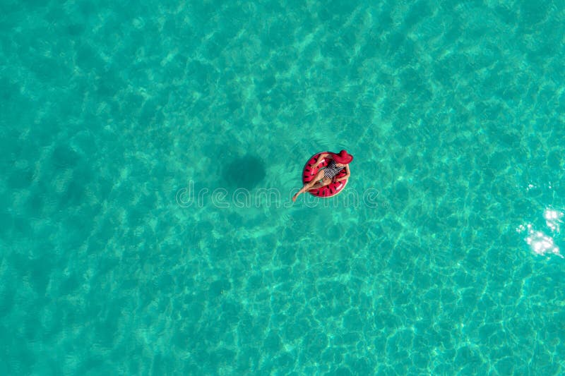 Aerial view of slim woman swimming on the swim ring donut in the transparent turquoise sea in Seychelles. Summer seascape with girl, beautiful waves, colorful water. Top view from drone. Aerial view of slim woman swimming on the swim ring donut in the transparent turquoise sea in Seychelles. Summer seascape with girl, beautiful waves, colorful water. Top view from drone