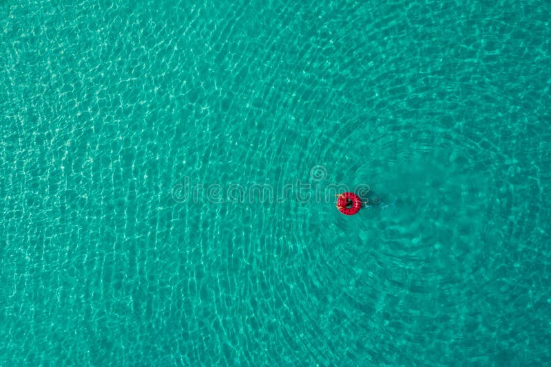 Aerial view of slim woman swimming on the swim ring donut in the transparent turquoise sea in Seychelles. Summer seascape with girl, beautiful waves, colorful water. Top view from drone. Aerial view of slim woman swimming on the swim ring donut in the transparent turquoise sea in Seychelles. Summer seascape with girl, beautiful waves, colorful water. Top view from drone