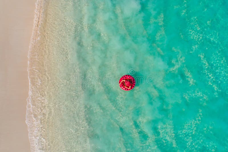 Aerial view of slim woman swimming on the swim ring donut in the transparent turquoise sea in Seychelles. Summer seascape with girl, beautiful waves, colorful water. Top view from drone. Aerial view of slim woman swimming on the swim ring donut in the transparent turquoise sea in Seychelles. Summer seascape with girl, beautiful waves, colorful water. Top view from drone