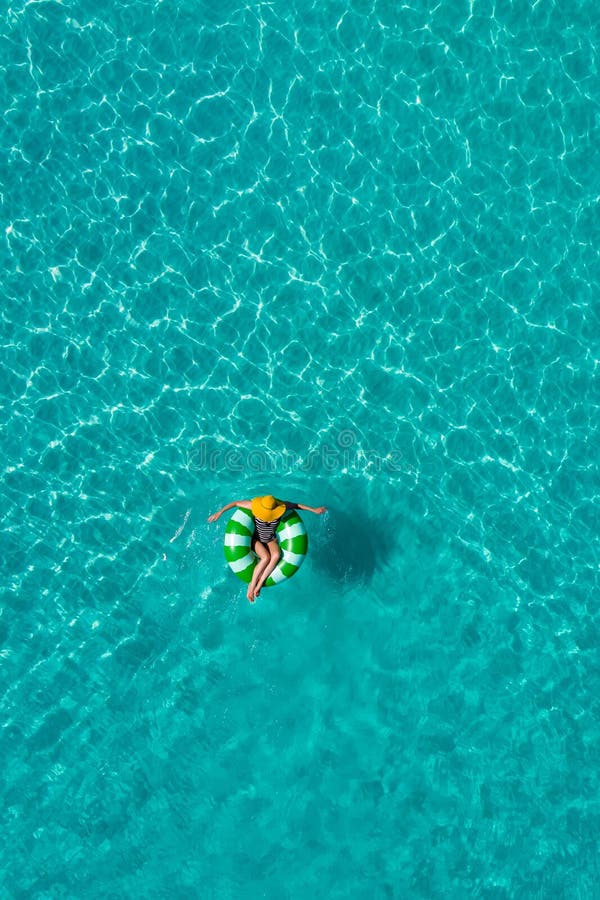 Aerial view of slim woman swimming on the swim ring donut in the transparent turquoise sea in Seychelles. Summer seascape with girl, beautiful waves, colorful water. Top view from drone. Aerial view of slim woman swimming on the swim ring donut in the transparent turquoise sea in Seychelles. Summer seascape with girl, beautiful waves, colorful water. Top view from drone