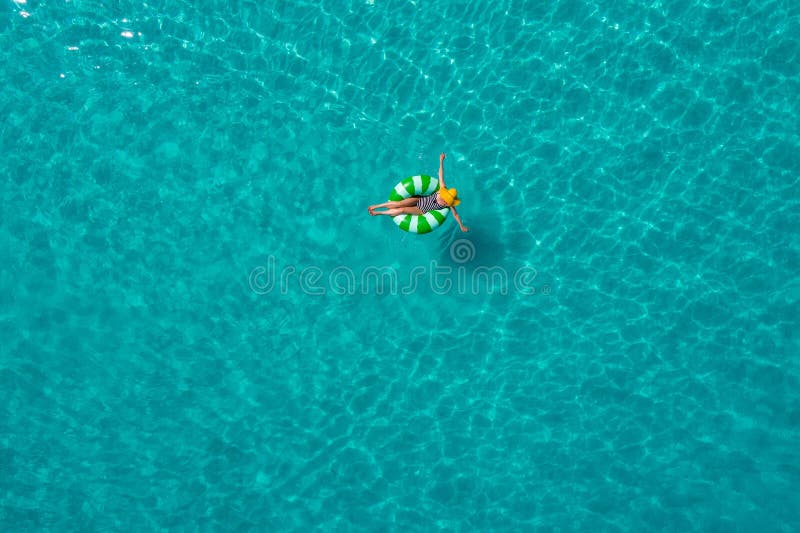 Aerial view of slim woman swimming on the swim ring donut in the transparent turquoise sea in Seychelles. Summer seascape with girl, beautiful waves, colorful water. Top view from drone. Aerial view of slim woman swimming on the swim ring donut in the transparent turquoise sea in Seychelles. Summer seascape with girl, beautiful waves, colorful water. Top view from drone