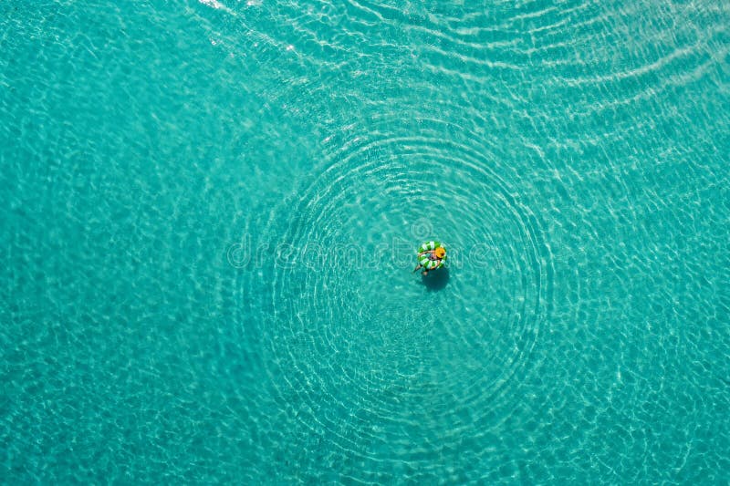 Aerial view of slim woman swimming on the swim ring donut in the transparent turquoise sea in Seychelles. Summer seascape with girl, beautiful waves, colorful water. Top view from drone. Aerial view of slim woman swimming on the swim ring donut in the transparent turquoise sea in Seychelles. Summer seascape with girl, beautiful waves, colorful water. Top view from drone