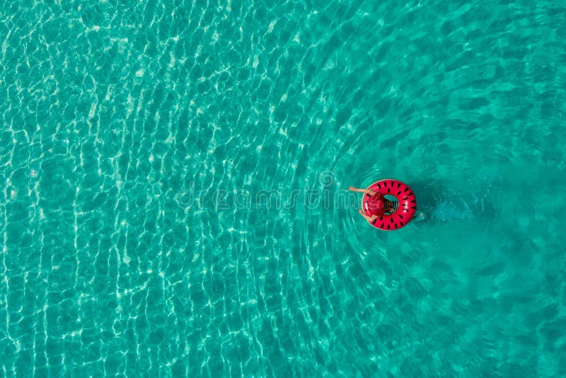 Aerial view of slim woman swimming on the swim ring donut in the transparent turquoise sea in Seychelles. Summer seascape with girl, beautiful waves, colorful water. Top view from drone. Aerial view of slim woman swimming on the swim ring donut in the transparent turquoise sea in Seychelles. Summer seascape with girl, beautiful waves, colorful water. Top view from drone