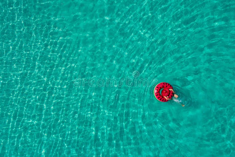 Aerial view of slim woman swimming on the swim ring donut in the transparent turquoise sea in Seychelles. Summer seascape with girl, beautiful waves, colorful water. Top view from drone. Aerial view of slim woman swimming on the swim ring donut in the transparent turquoise sea in Seychelles. Summer seascape with girl, beautiful waves, colorful water. Top view from drone