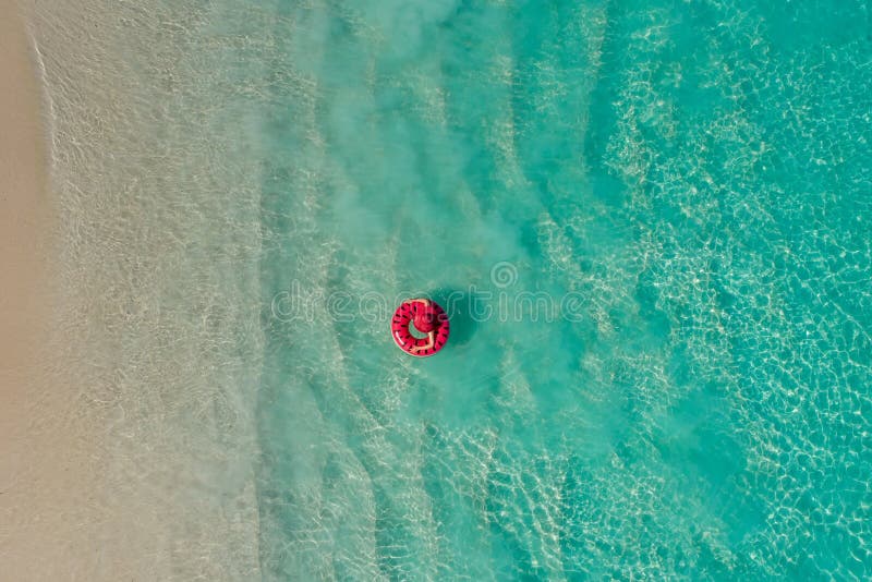 Aerial view of slim woman swimming on the swim ring donut in the transparent turquoise sea in Seychelles. Summer seascape with girl, beautiful waves, colorful water. Top view from drone. Aerial view of slim woman swimming on the swim ring donut in the transparent turquoise sea in Seychelles. Summer seascape with girl, beautiful waves, colorful water. Top view from drone