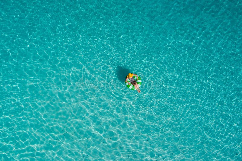 Aerial view of slim woman swimming on the swim ring donut in the transparent turquoise sea in Seychelles. Summer seascape with girl, beautiful waves, colorful water. Top view from drone. Aerial view of slim woman swimming on the swim ring donut in the transparent turquoise sea in Seychelles. Summer seascape with girl, beautiful waves, colorful water. Top view from drone