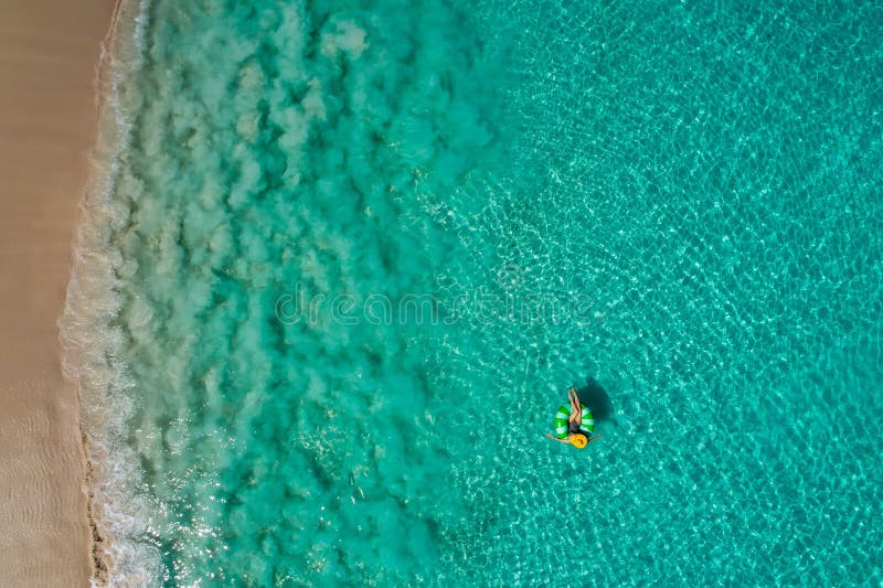 Aerial view of slim woman swimming on the swim ring donut in the transparent turquoise sea in Seychelles. Summer seascape with girl, beautiful waves, colorful water. Top view from drone. Aerial view of slim woman swimming on the swim ring donut in the transparent turquoise sea in Seychelles. Summer seascape with girl, beautiful waves, colorful water. Top view from drone