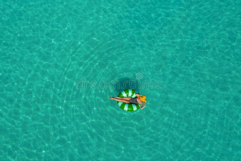 Aerial view of slim woman swimming on the swim ring donut in the transparent turquoise sea in Seychelles. Summer seascape with girl, beautiful waves, colorful water. Top view from drone. Aerial view of slim woman swimming on the swim ring donut in the transparent turquoise sea in Seychelles. Summer seascape with girl, beautiful waves, colorful water. Top view from drone